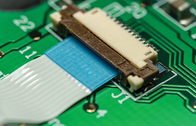 Macro photo of a flat ribbon cable and connector on a green printed circuit board (PCB)