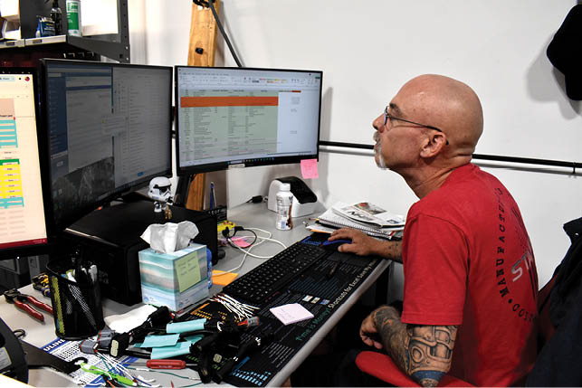A man with a bald head is sitting at a desk with a keyboard and two computer monitors. Description generated by AI