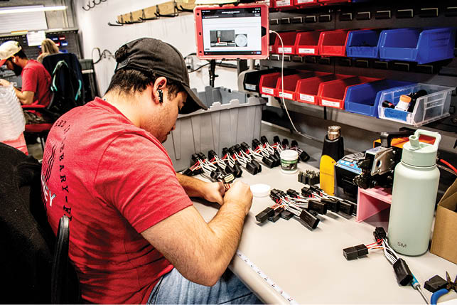 A man wearing a red shirt is working on a table with electronic equipment. Description generated by AI