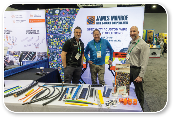 A group of men standing in front of a table with a sign that says James Monroe & Co. Custom Wire. Description generated by AI