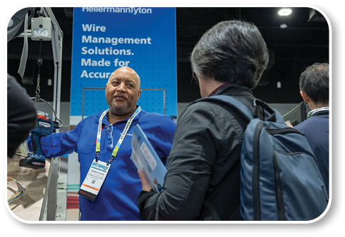 A man wearing a blue shirt is standing in front of a sign. Description generated by AI