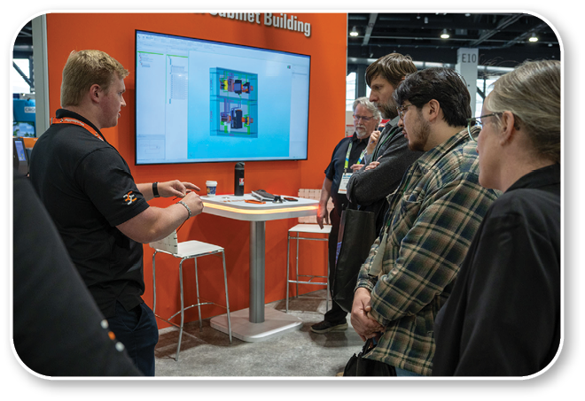 A group of people are standing around a table with a computer monitor on it. Description generated by AI