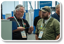 Two men wearing lanyards are talking to each other. Description generated by AI