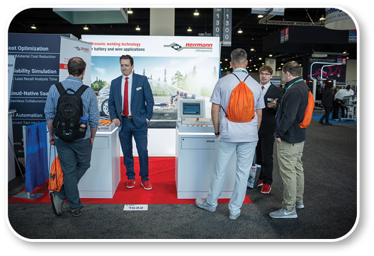A man in a suit is standing next to a table with a laptop and a man in a white shirt is standing next to him. Description generated by AI