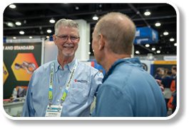 Two men wearing name tags are talking to each other. Description generated by AI