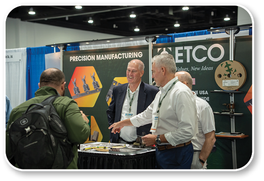 A group of men are standing around a table with a sign that says “Precision Manufacturing." Description generated by AI