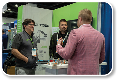 Three men are standing in front of a table with a sign that says “Solutions". Description generated by AI