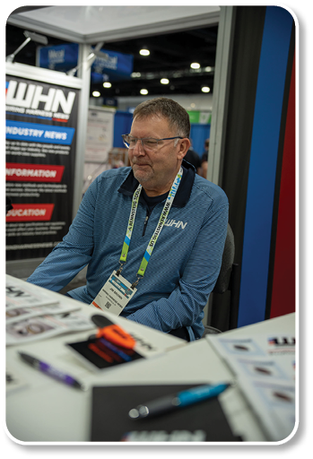 A man wearing a name tag is sitting at a table. Description generated by AI
