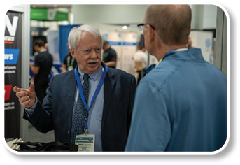 A man wearing a blue lanyard and a suit is talking to another man. Description generated by AI